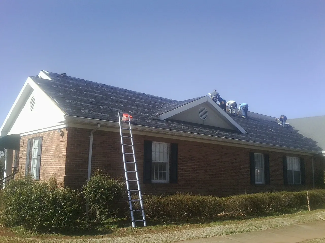 Crew tearing shingles off a brick ranch roof with a ladder set — Metal Roof Repair work by our crew in Harrisburg